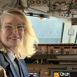 A person with glasses and blonde hair is smiling in the cockpit of an aircraft.