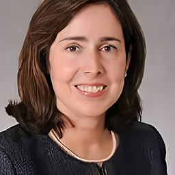 A person with shoulder-length brown hair wearing a dark jacket smiles against a neutral background.